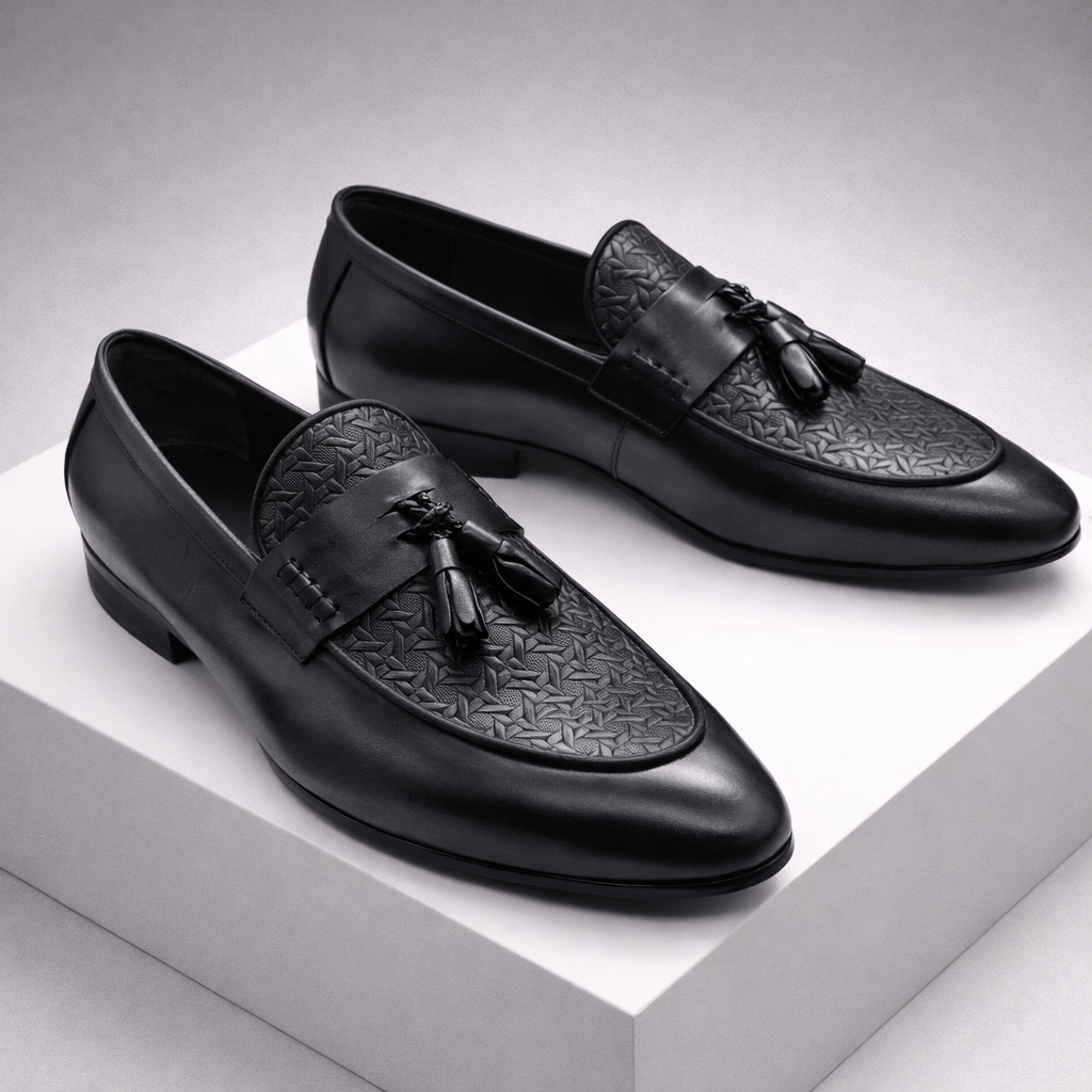 Black leather tassel loafer dress shoes for men with embossed toe cap and slip-on design, displayed on white platform.