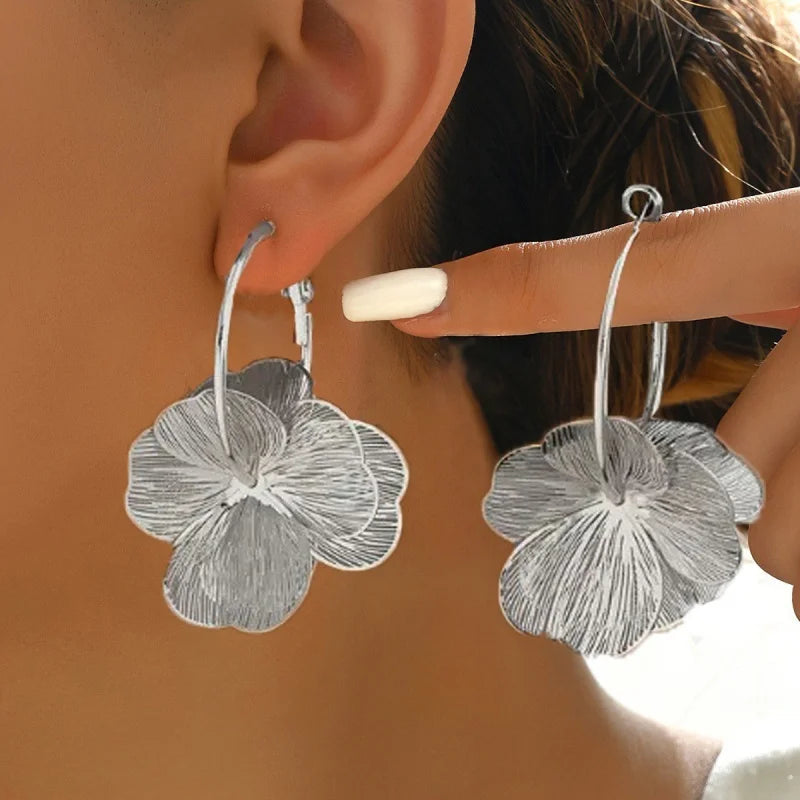 Silver textured flower hoop earrings worn by a woman, featuring detailed petal design with brushed metallic finish