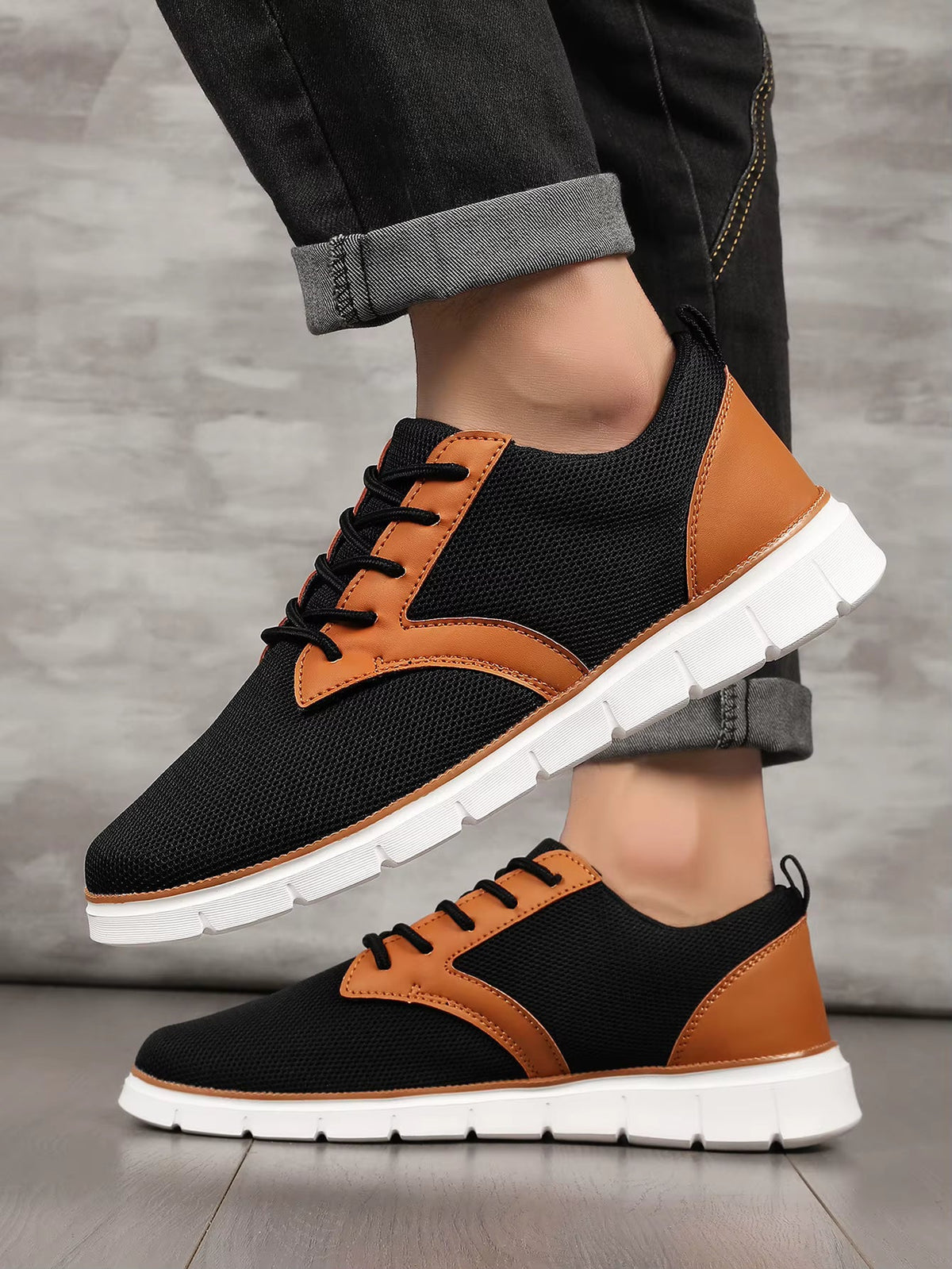 Black and tan canvas leather orthopedic sneakers with white sole, lace-up style, worn with rolled dark jeans.