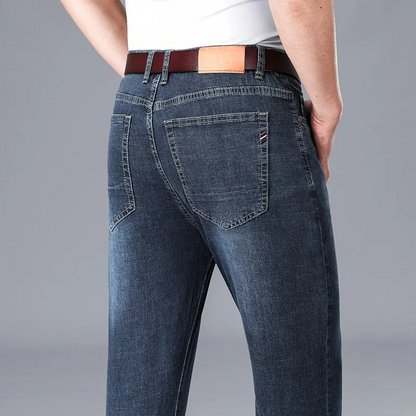 Back view of men's stretch slim-fit dark blue denim jeans with back pockets, brown leather belt, and white t-shirt.
