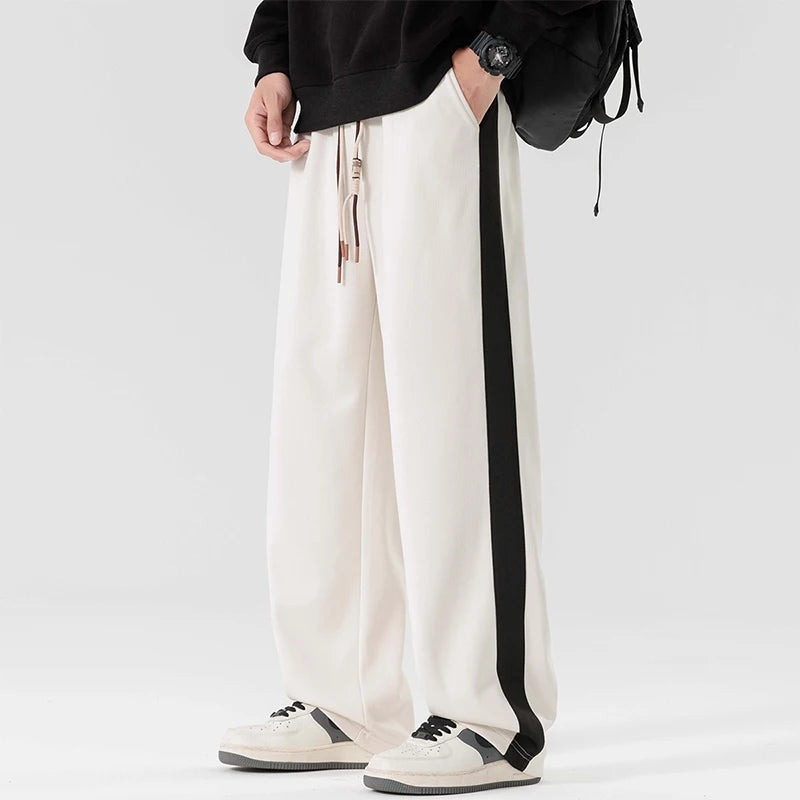 Men's white wide-leg sweatpants with black side stripe, drawstring waist, paired with black hoodie and white sneakers
