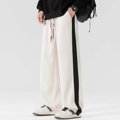Men's white wide-leg sweatpants with black side stripe, drawstring waist, paired with black hoodie and white sneakers
