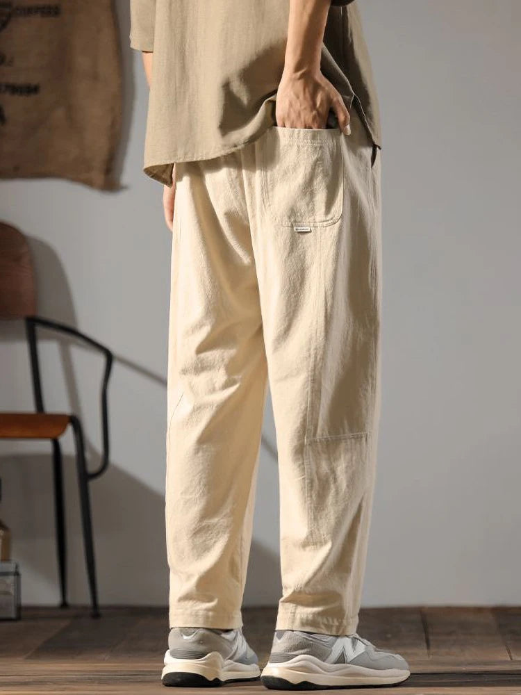 Men's wide-leg beige linen drawstring pants paired with gray sneakers, relaxed fit with side pockets, casual style