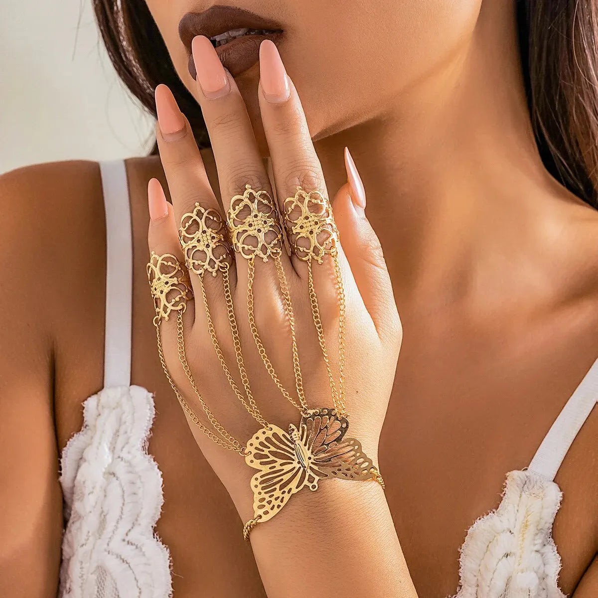 Gold butterfly hand chain bracelet with filigree finger rings connected by delicate chains, worn on woman's hand.