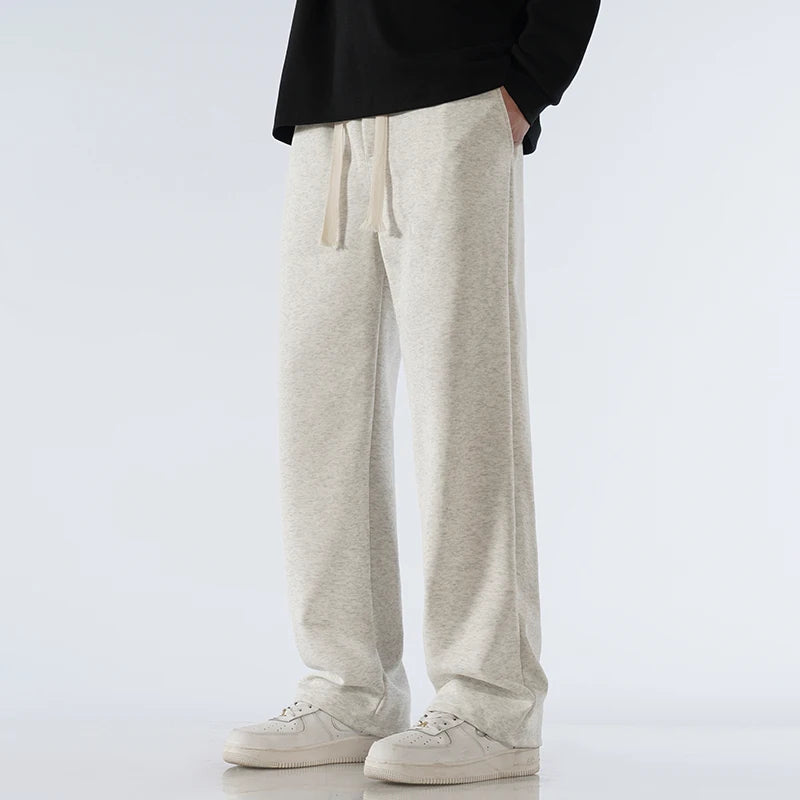 Man wearing light gray cotton wide-leg relaxed-fit drawstring sweatpants with white sneakers and black top.