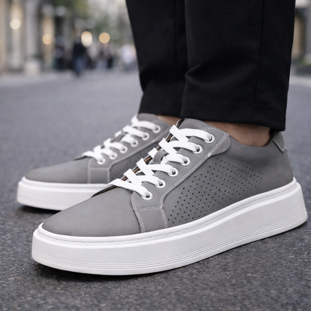 Men's gray leather lace-up sneakers with perforated side detail and white sole, styled with black trousers on pavement.