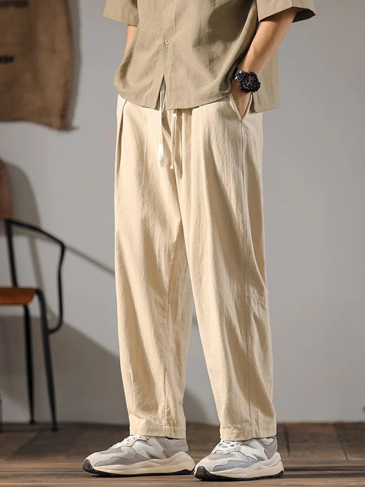 Men's beige wide-leg linen drawstring pants with relaxed fit, paired with white sneakers and casual shirt