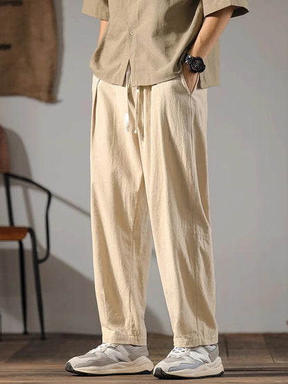 Men's beige wide-leg linen drawstring pants with relaxed fit, paired with white sneakers and casual shirt