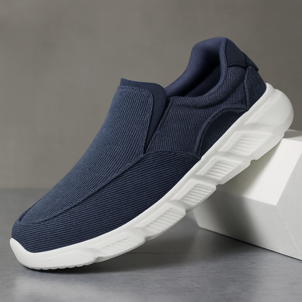Navy blue corduroy slip-on sneakers for men with white chunky sole, displayed against a gray background.