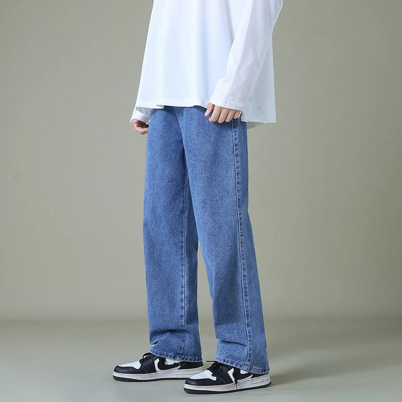 Man wearing relaxed-fit straight-leg blue denim jeans paired with a white long-sleeve shirt and black sneakers.