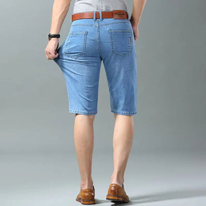 Men's light blue stretch denim shorts with brown leather belt, back pockets, worn with tan loafers, rear view.