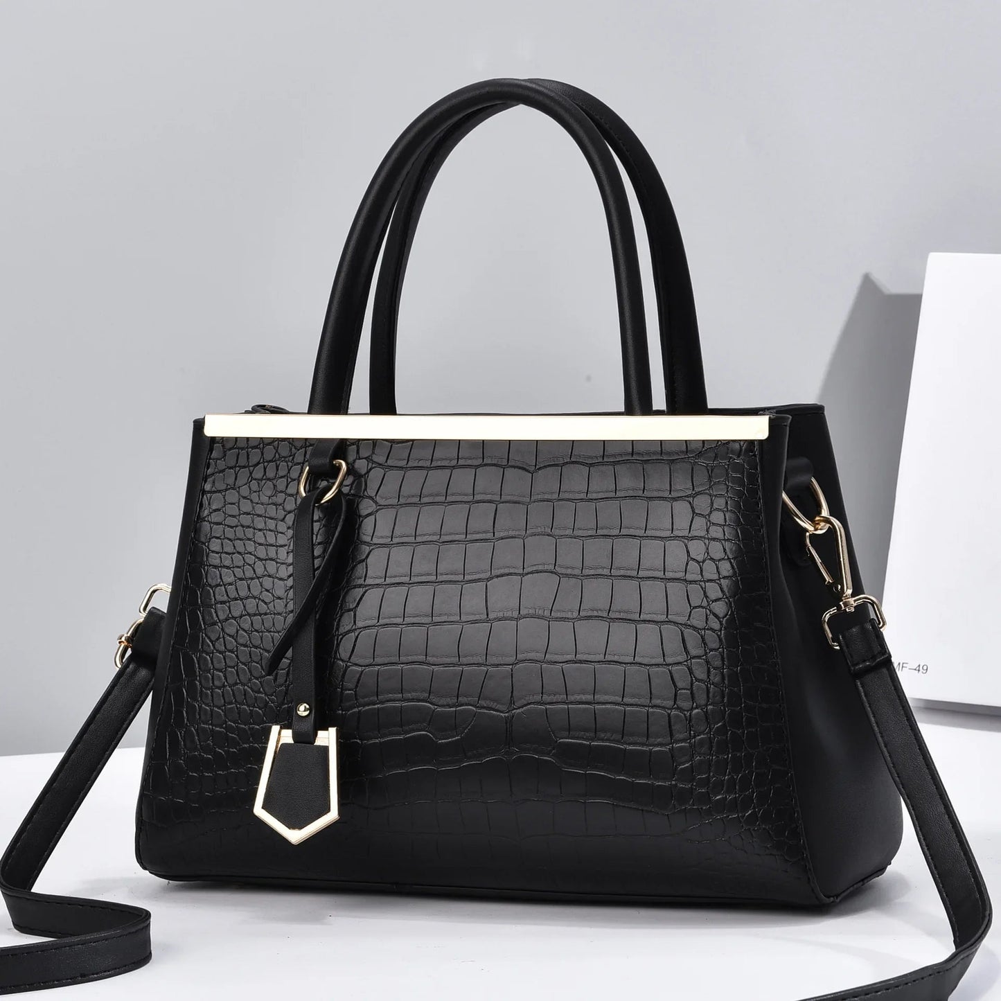 Black croc-embossed structured handbag with gold-tone bar detail, dual top handles, decorative charm, and removable crossbody strap.