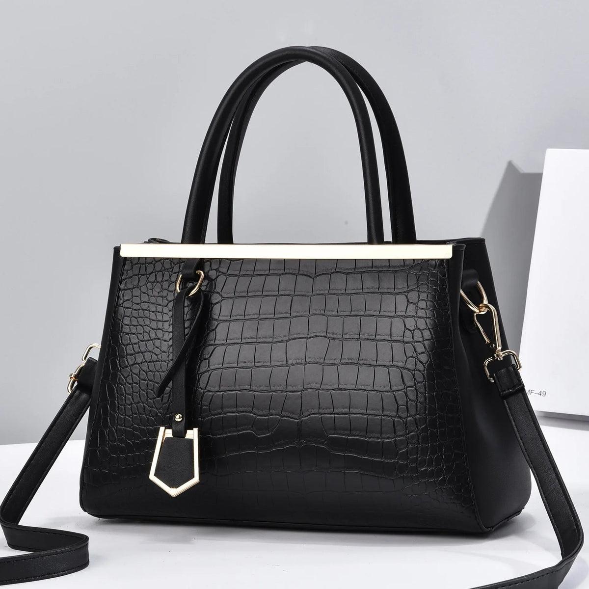 Black croc-embossed structured handbag with gold-tone bar detail, dual top handles, decorative charm, and removable crossbody strap.