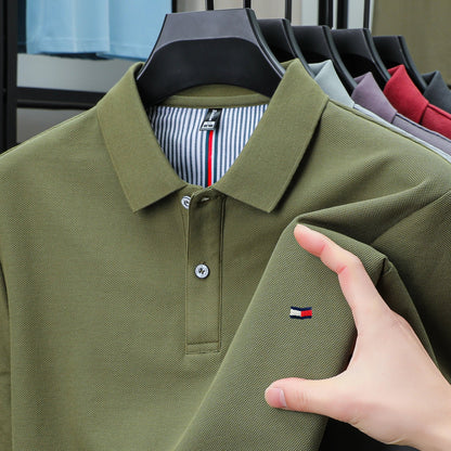 Army green men's cotton polo shirt with small flag logo, displayed on hanger among other color variants.