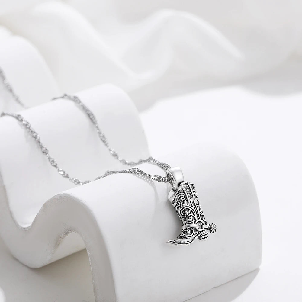 Silver necklace with intricate filigree western cowboy boot charm pendant on delicate chain, displayed on white prop
