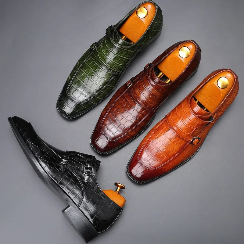 Four men's crocodile-pattern leather double monk strap dress shoes in green, brown, tan, and black colors with shoe trees inserted.