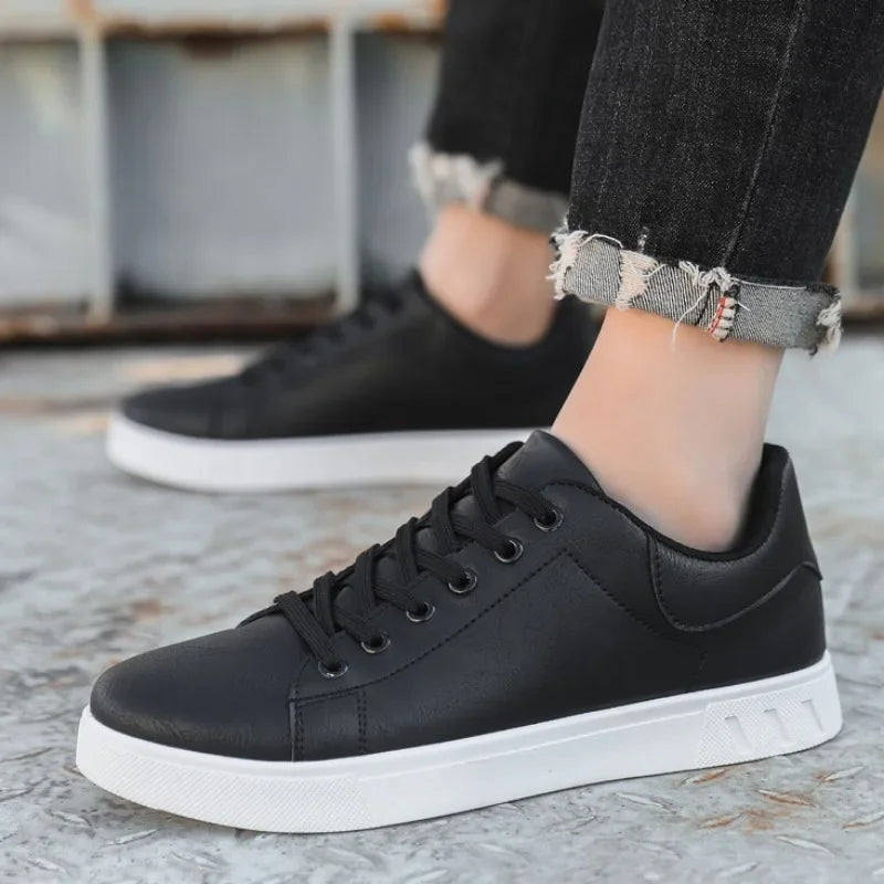 Black leather lace-up low-top sneakers with white sole, worn with distressed black jeans on concrete surface.