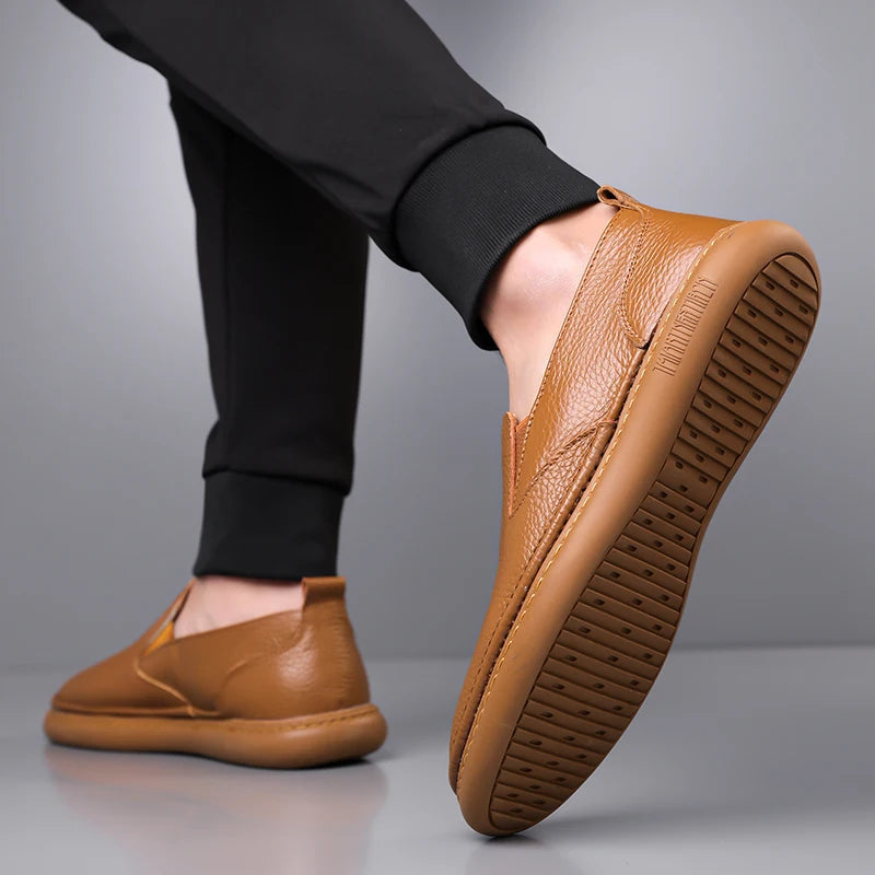 Brown leather slip-on loafers with textured rubber sole worn with black jogger pants, shown from side angle