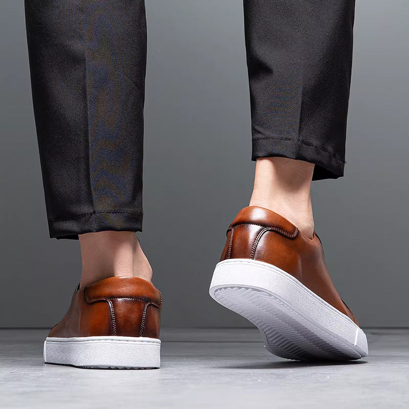 Men's brown leather slip-on sneakers with white platform sole, shown from behind with dark trousers.