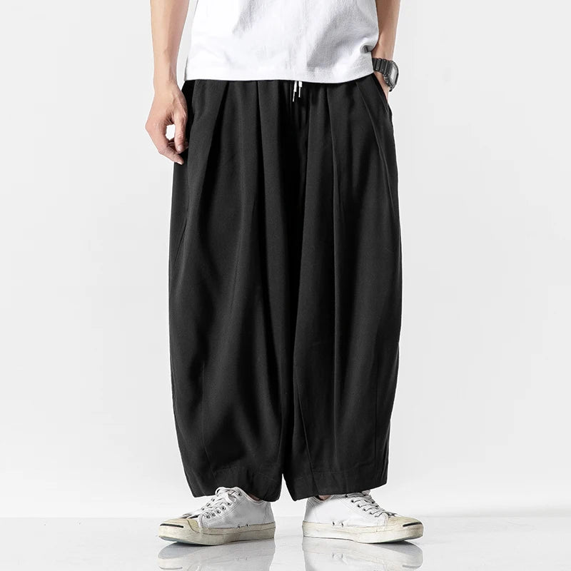 Man wearing black wide-leg cotton drawstring harem pants with elastic ankles, paired with white sneakers and t-shirt.