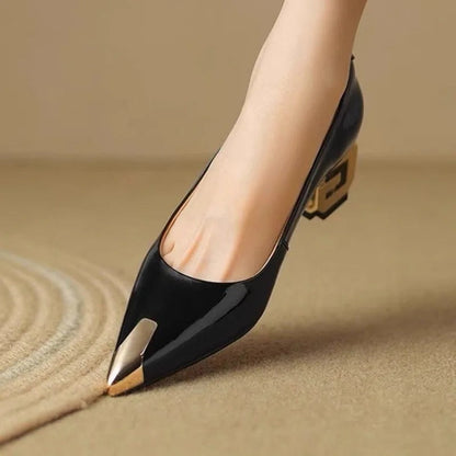 Black patent leather block heel pumps with gold metal pointed toe cap and decorative chunky heel on woman's foot