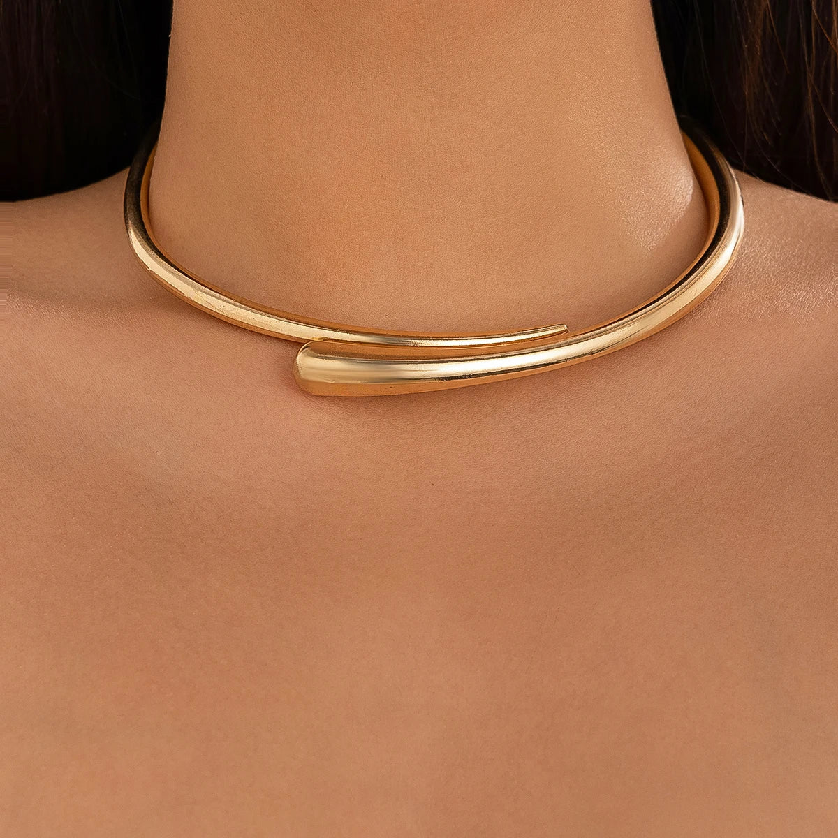 Gold tone open cuff choker necklace with overlapping tapered ends worn around a woman's neck