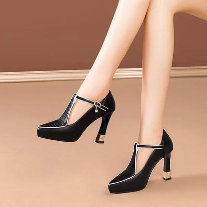 Black T-strap block heel pumps with gold trim and rhinestone accent, shown on model's feet against warm beige background.