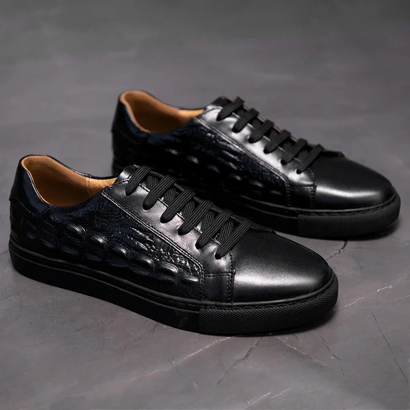 Black men's leather lace-up sneakers with crocodile embossed detail and tan interior lining on gray background