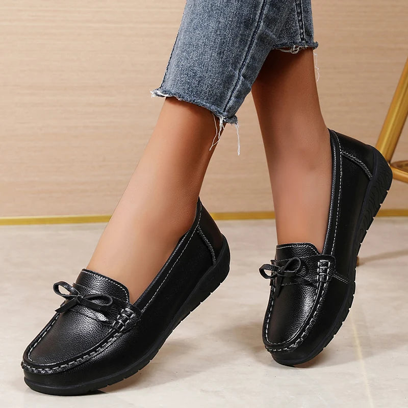 Black leather slip-on bow loafers worn with cropped jeans, featuring decorative bow detail and contrast stitching