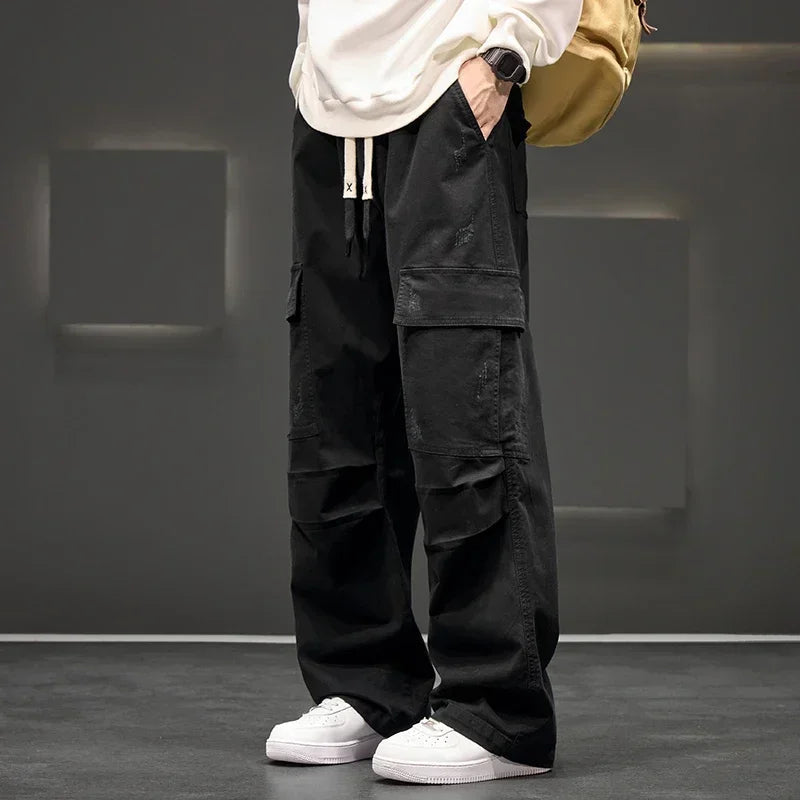 Black wide-leg men's cargo pants with multiple pockets, drawstring waist, paired with white sneakers and cream sweatshirt