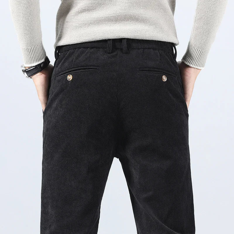 Back view of men's black corduroy slim fit pants with button back pockets, paired with a cream knit sweater.