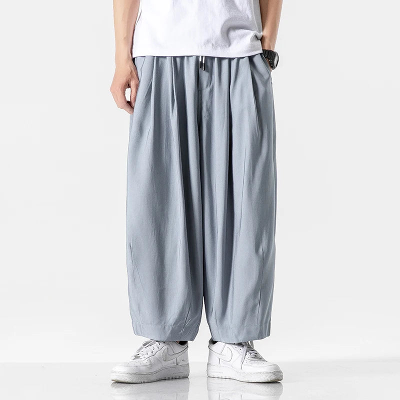 Men's wide-leg gray cotton drawstring pants with pleated front, elastic waist, worn with white sneakers and t-shirt