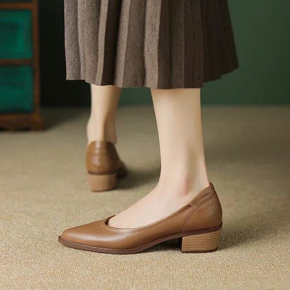 Women's brown leather pointed-toe mid-heel pumps with block heel, styled with a brown midi skirt on beige carpet.