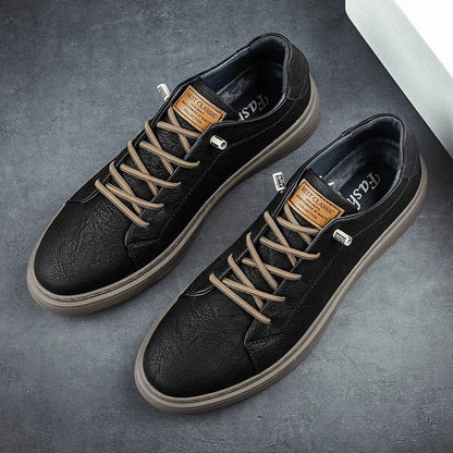 Black leather low-top men's sneakers with tan laces, brown label, and gum sole on gray background