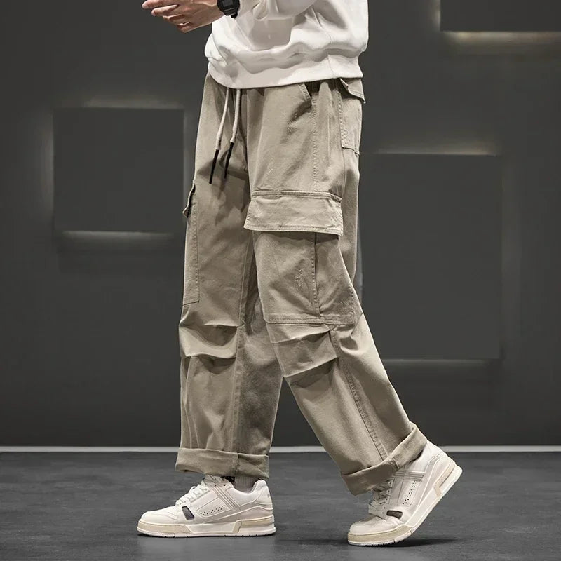 Men's wide-leg khaki cargo pants with multiple side pockets, drawstring waist, worn with white sneakers and sweatshirt
