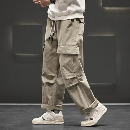 Men's wide-leg khaki cargo pants with multiple side pockets, drawstring waist, worn with white sneakers and sweatshirt