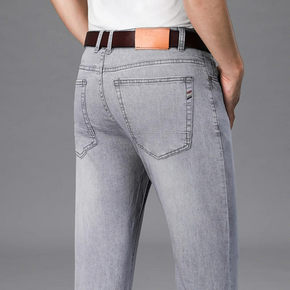 Men's light gray stretch slim-fit denim jeans shown from back, featuring brown leather belt and rear pocket detail.