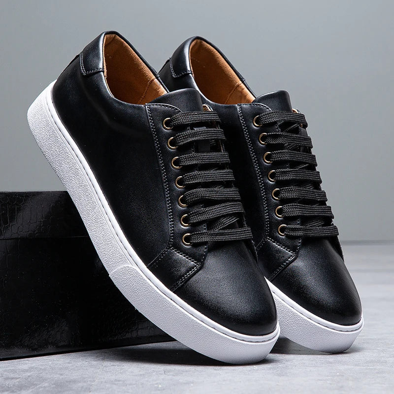 Black leather lace-up men's sneakers with gold eyelets, white rubber sole, and tan interior lining displayed on shoebox