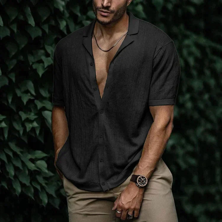 Man wearing black short sleeve button-down linen shirt with camp collar, paired with khaki pants and watch.