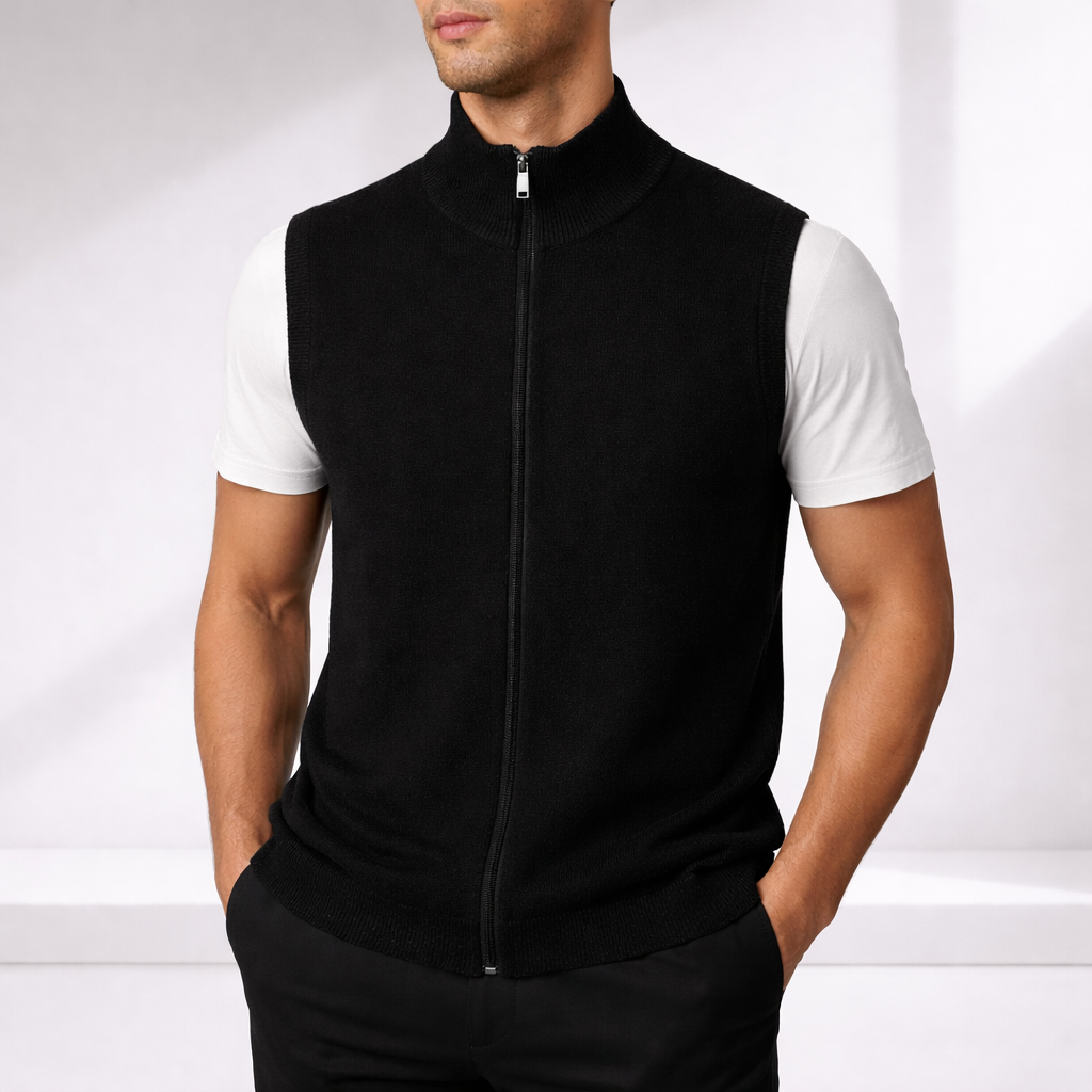 Man wearing a black merino wool full zip-up vest over a white t-shirt with black pants, hands in pockets.