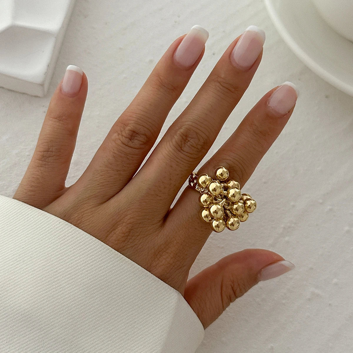 Gold beaded cluster adjustable ring on woman's hand with neutral manicure against white background