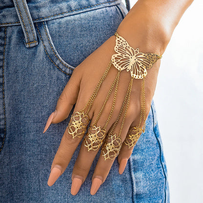 Gold butterfly hand chain bracelet connected to four ornate filigree rings worn on a woman's hand against denim jeans.