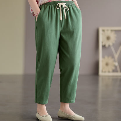 Women's green linen tapered pants with elastic drawstring waist, side pockets, and cropped ankles, paired with sage flats.