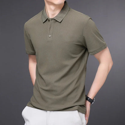 Men's olive green short-sleeve cotton polo shirt with collar and button placket, paired with white pants.