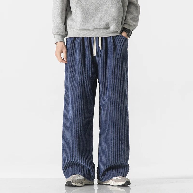 Men's wide-leg navy blue corduroy drawstring pants paired with a gray sweatshirt and white sneakers, casual streetwear style.
