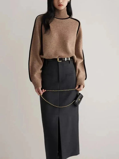 Woman wearing camel turtleneck ribbed sweater with black contrast piping, paired with black midi skirt and belt.