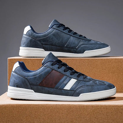 Navy blue men's low-top sneakers with white stripe detail and cream sole on cork display box