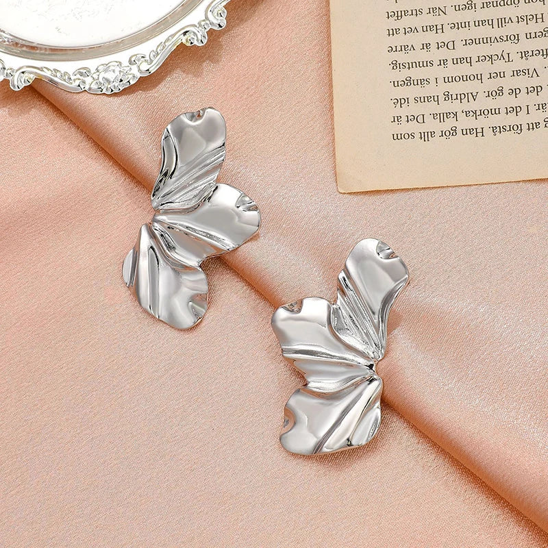 Silver tone ruffled statement drop earrings with textured wave design displayed on pink satin fabric