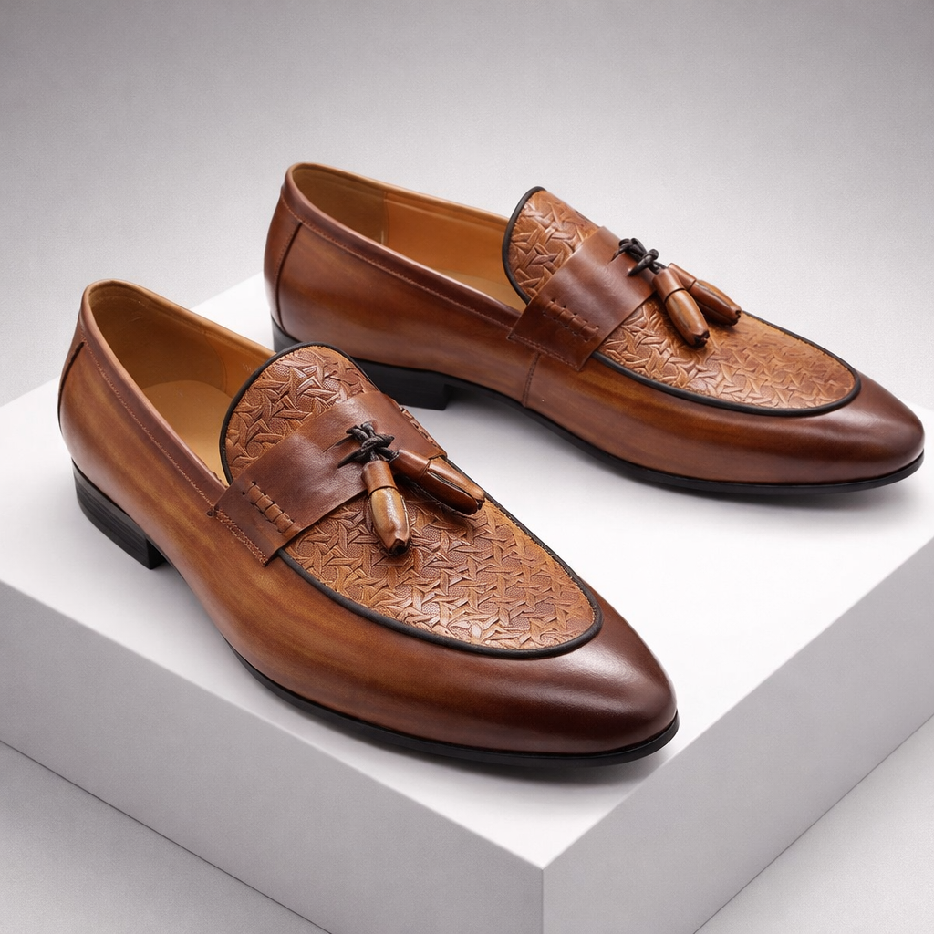Brown leather tassel loafer dress shoes for men with embossed toe detail and slip-on design, displayed on white platform.