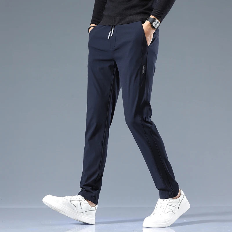 Man wearing navy blue cotton drawstring joggers with side stripe, paired with black sweater and white sneakers.